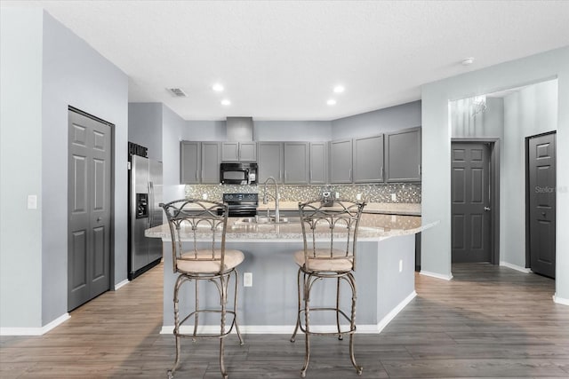 kitchen featuring a kitchen breakfast bar, gray cabinets, an island with sink, light stone countertops, and black appliances