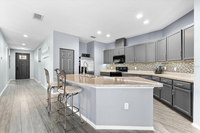 kitchen featuring gray cabinetry, light wood-type flooring, black appliances, and a center island with sink