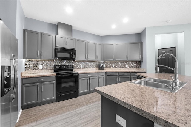 kitchen featuring sink, gray cabinetry, light hardwood / wood-style floors, decorative backsplash, and black appliances