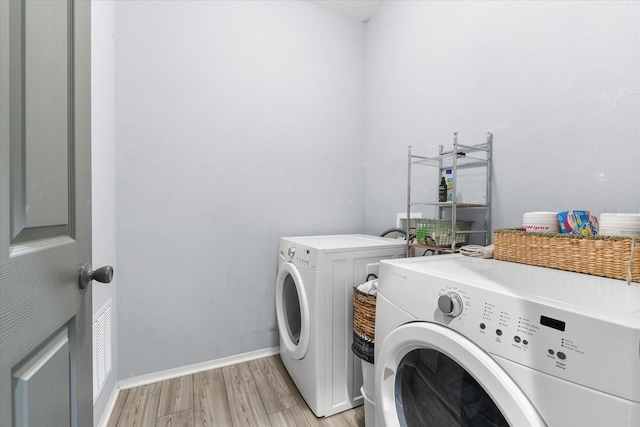 clothes washing area with washing machine and clothes dryer and light wood-type flooring