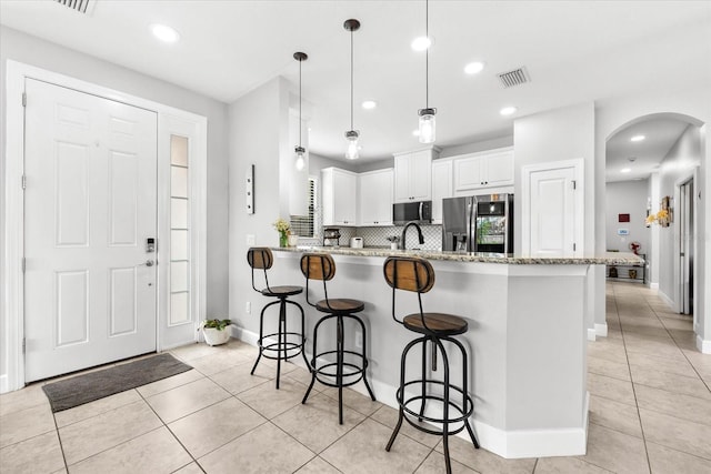 kitchen featuring white cabinetry, kitchen peninsula, light tile patterned flooring, stainless steel refrigerator, and light stone counters