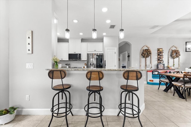 kitchen featuring white cabinets, a breakfast bar, appliances with stainless steel finishes, and pendant lighting