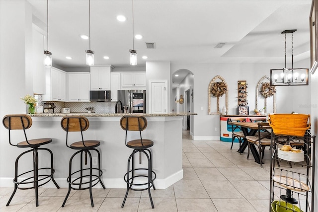 kitchen with decorative light fixtures, a breakfast bar, stainless steel appliances, white cabinets, and light stone counters