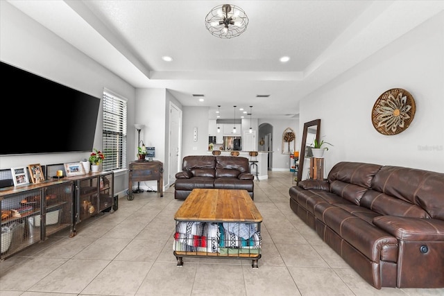 tiled living room featuring a raised ceiling and a notable chandelier