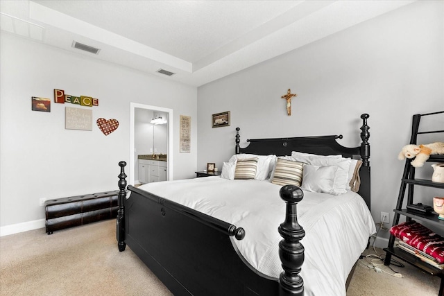 carpeted bedroom featuring a tray ceiling and ensuite bath