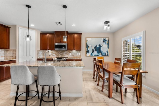 kitchen featuring sink, pendant lighting, light stone countertops, a kitchen island with sink, and decorative backsplash