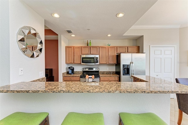 kitchen with a breakfast bar, light stone counters, ornamental molding, and appliances with stainless steel finishes