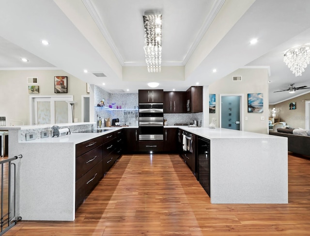 kitchen featuring a raised ceiling, decorative backsplash, dark brown cabinetry, and kitchen peninsula