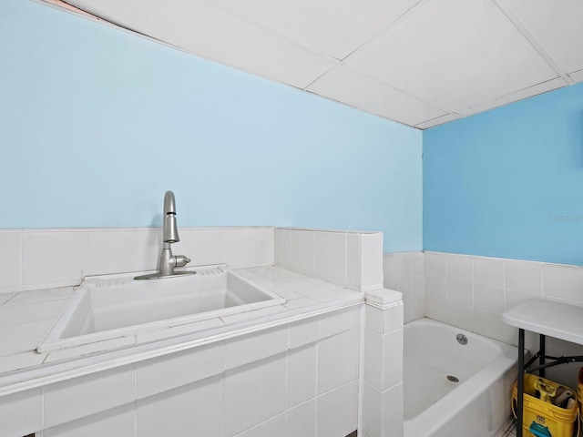 bathroom with a paneled ceiling, a bathtub, and sink