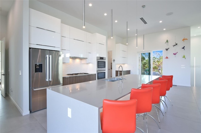 kitchen featuring modern cabinets, appliances with stainless steel finishes, a sink, white cabinetry, and backsplash