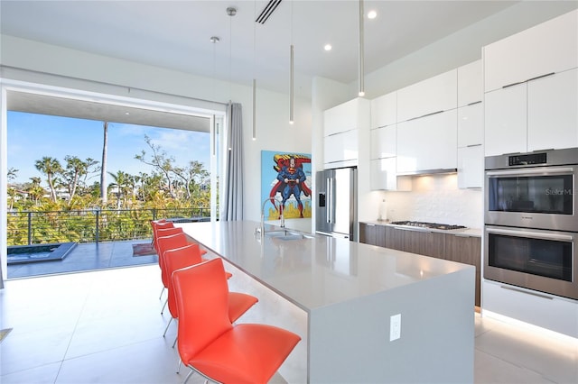 kitchen featuring stainless steel appliances, decorative backsplash, a sink, an island with sink, and modern cabinets