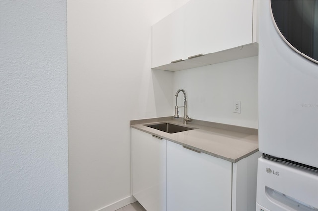 kitchen with light countertops, a sink, stacked washer and clothes dryer, and white cabinetry