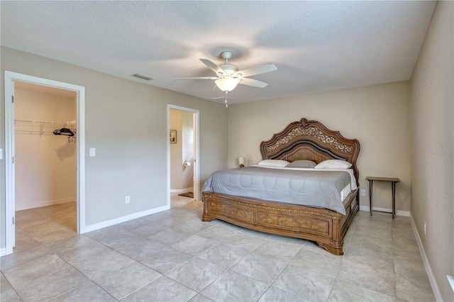 bedroom with a walk in closet, ceiling fan, a textured ceiling, ensuite bath, and a closet