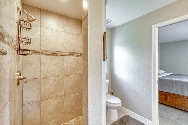 bathroom with toilet, tile patterned flooring, and a tile shower