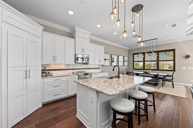 kitchen featuring white cabinetry, stainless steel appliances, hanging light fixtures, and an island with sink