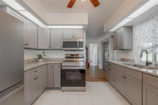 kitchen featuring light stone countertops, sink, stainless steel appliances, gray cabinets, and light tile patterned floors