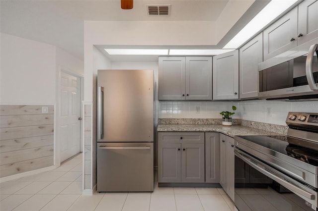 kitchen featuring light stone countertops, appliances with stainless steel finishes, tasteful backsplash, gray cabinetry, and light tile patterned flooring