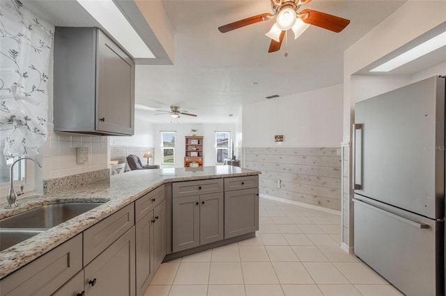 kitchen featuring stainless steel refrigerator, light stone countertops, sink, gray cabinetry, and kitchen peninsula