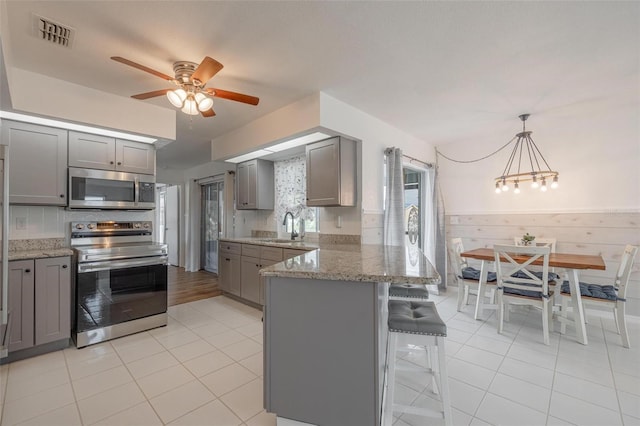 kitchen featuring light stone countertops, gray cabinetry, stainless steel appliances, sink, and pendant lighting