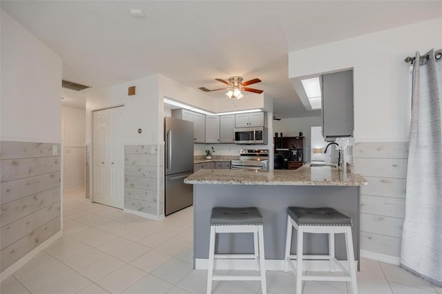 kitchen featuring kitchen peninsula, appliances with stainless steel finishes, light stone counters, gray cabinets, and light tile patterned flooring