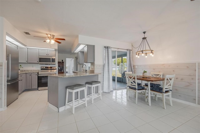 kitchen with light stone counters, decorative light fixtures, gray cabinets, light tile patterned floors, and appliances with stainless steel finishes