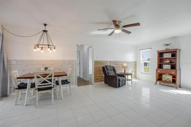 unfurnished dining area with wood walls, light tile patterned flooring, and ceiling fan with notable chandelier