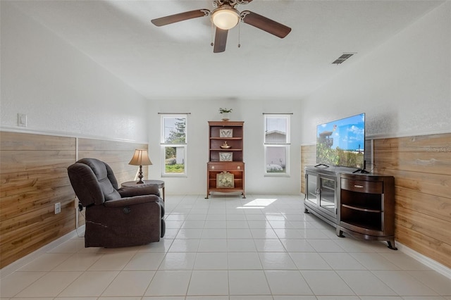 sitting room with wooden walls, light tile patterned floors, and ceiling fan