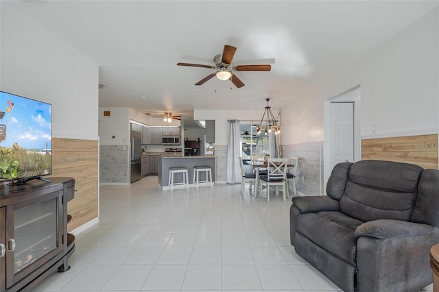 living room with wood walls, light tile patterned floors, and ceiling fan with notable chandelier