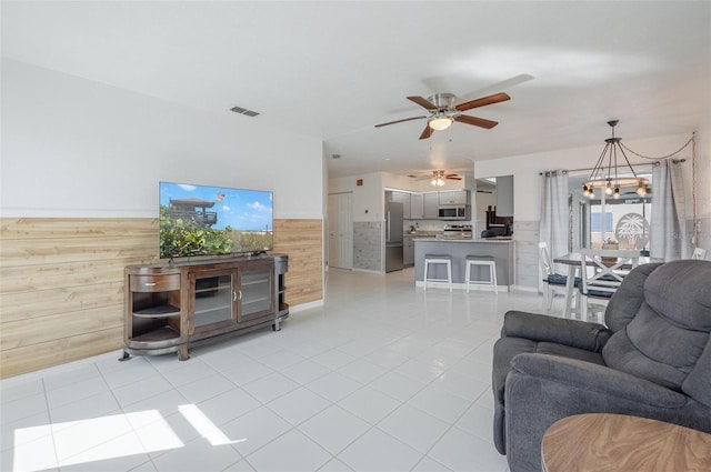 living room featuring wooden walls, light tile patterned flooring, and ceiling fan with notable chandelier