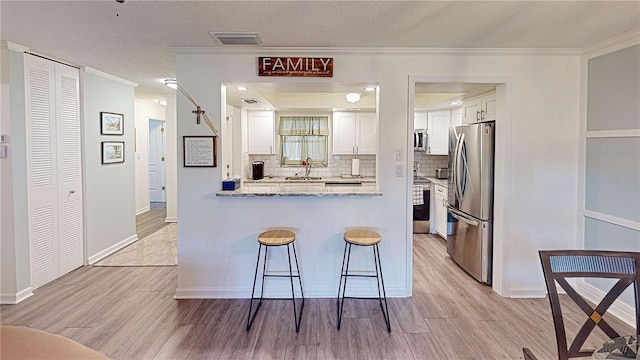 kitchen featuring crown molding, light stone countertops, white cabinetry, and stainless steel appliances