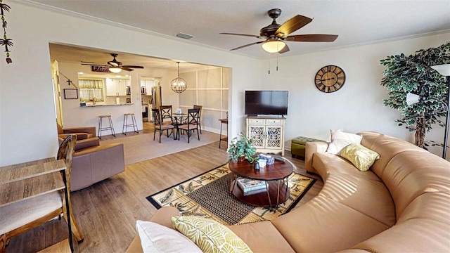 living room with wood-type flooring, ceiling fan with notable chandelier, and crown molding