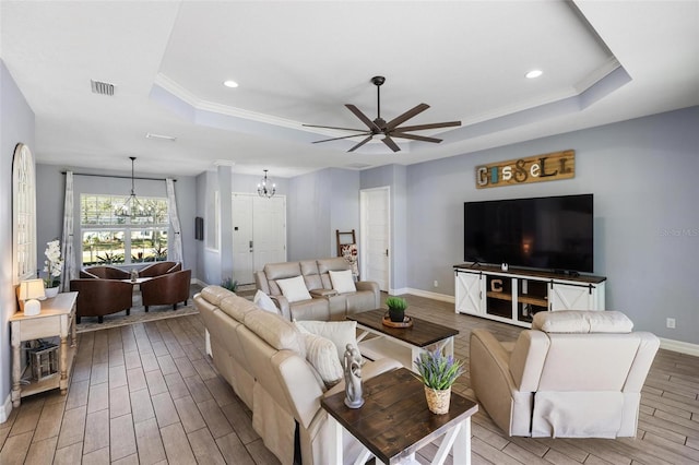 living room featuring ceiling fan with notable chandelier, a raised ceiling, and ornamental molding