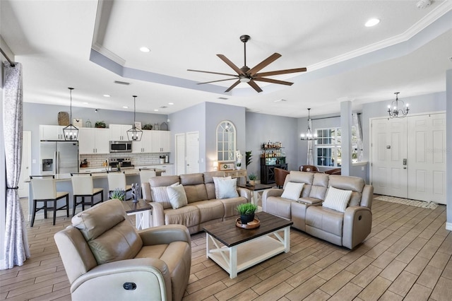 living room with ceiling fan with notable chandelier, a raised ceiling, and ornamental molding