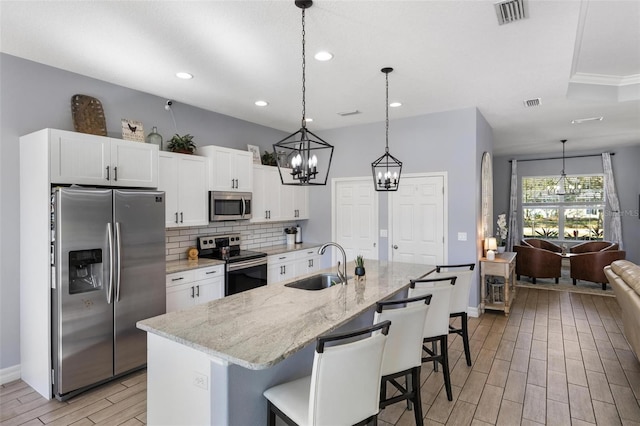 kitchen with white cabinets, sink, an island with sink, light stone counters, and stainless steel appliances