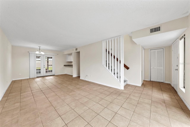 unfurnished living room with a notable chandelier, light tile patterned floors, a textured ceiling, and french doors