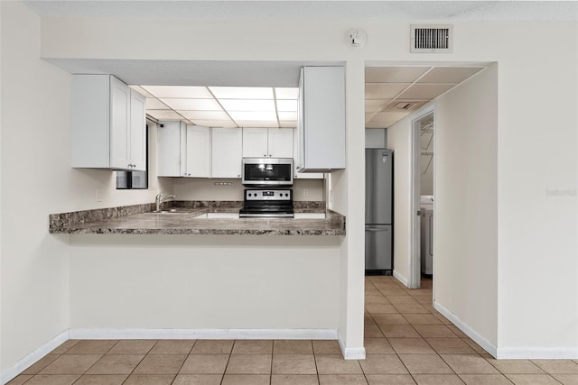 kitchen with stainless steel appliances, sink, light tile patterned floors, dark stone countertops, and white cabinetry