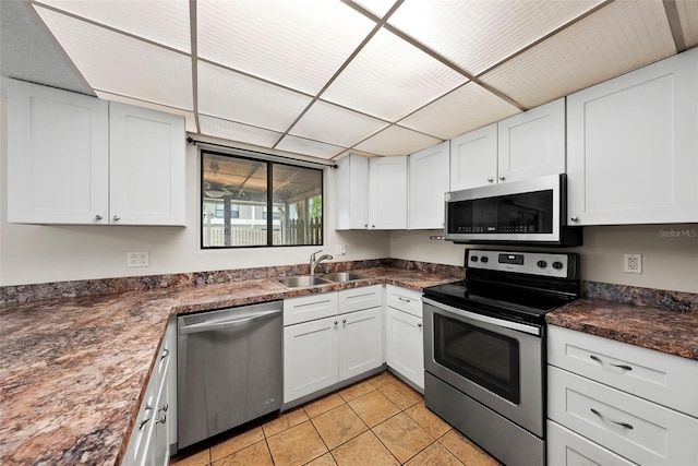 kitchen with appliances with stainless steel finishes, a drop ceiling, sink, light tile patterned floors, and white cabinets