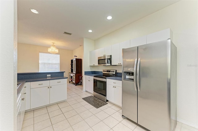 kitchen featuring light tile patterned floors, dark countertops, a peninsula, stainless steel appliances, and white cabinetry