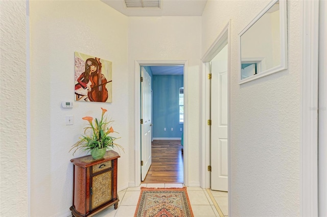 corridor featuring baseboards, visible vents, and light tile patterned flooring