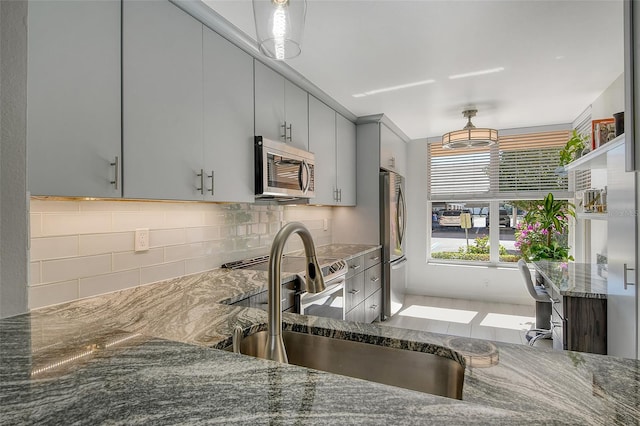 kitchen featuring appliances with stainless steel finishes, dark stone countertops, gray cabinetry, and sink