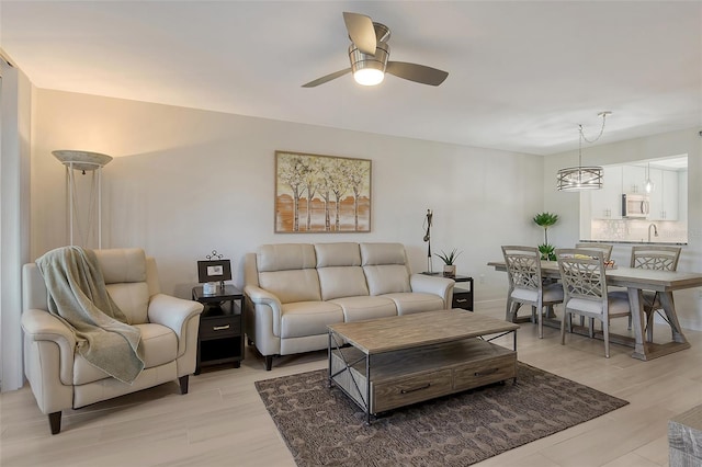 living room with ceiling fan with notable chandelier and light hardwood / wood-style flooring