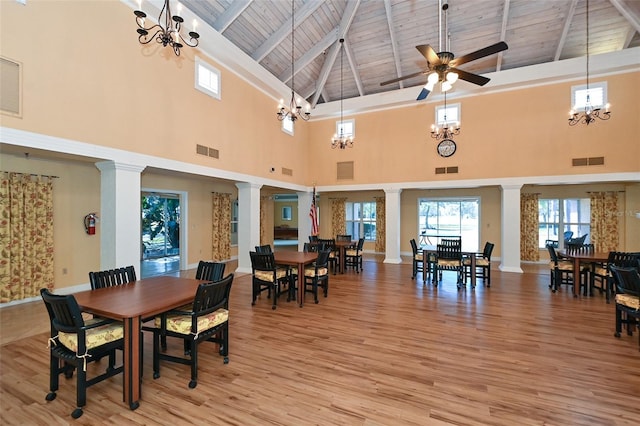 dining space with ceiling fan, a high ceiling, beamed ceiling, decorative columns, and light hardwood / wood-style floors