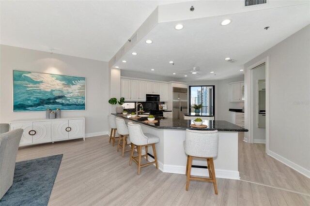 kitchen with a kitchen breakfast bar, white cabinets, light hardwood / wood-style floors, and black appliances