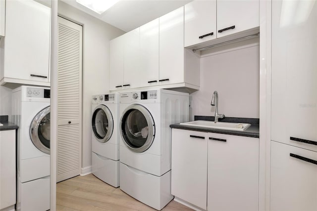 washroom with independent washer and dryer, sink, light hardwood / wood-style flooring, and cabinets