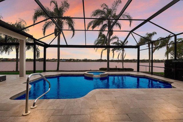 pool at dusk with an in ground hot tub, a water view, glass enclosure, and a patio area