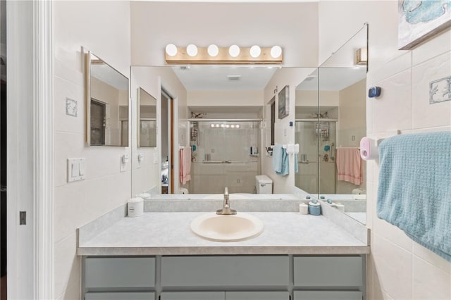 bathroom with vanity, toilet, an enclosed shower, and tile walls