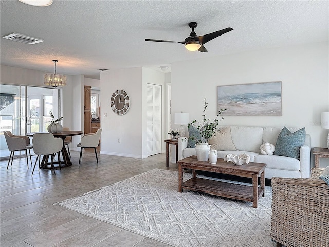 living room featuring ceiling fan with notable chandelier and a textured ceiling