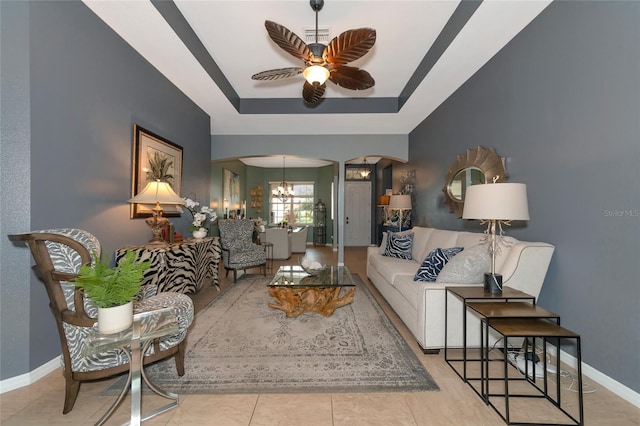 living room with ceiling fan with notable chandelier, light tile patterned flooring, and a tray ceiling