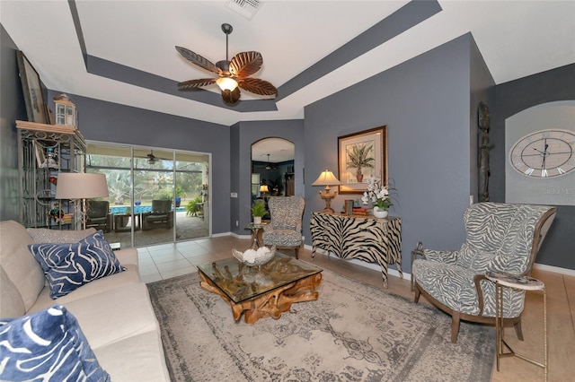 tiled living room featuring ceiling fan and a raised ceiling