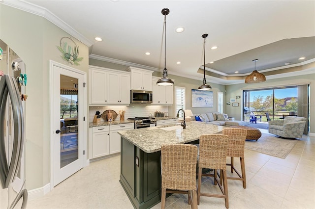 kitchen featuring appliances with stainless steel finishes, a center island with sink, light stone counters, sink, and white cabinetry